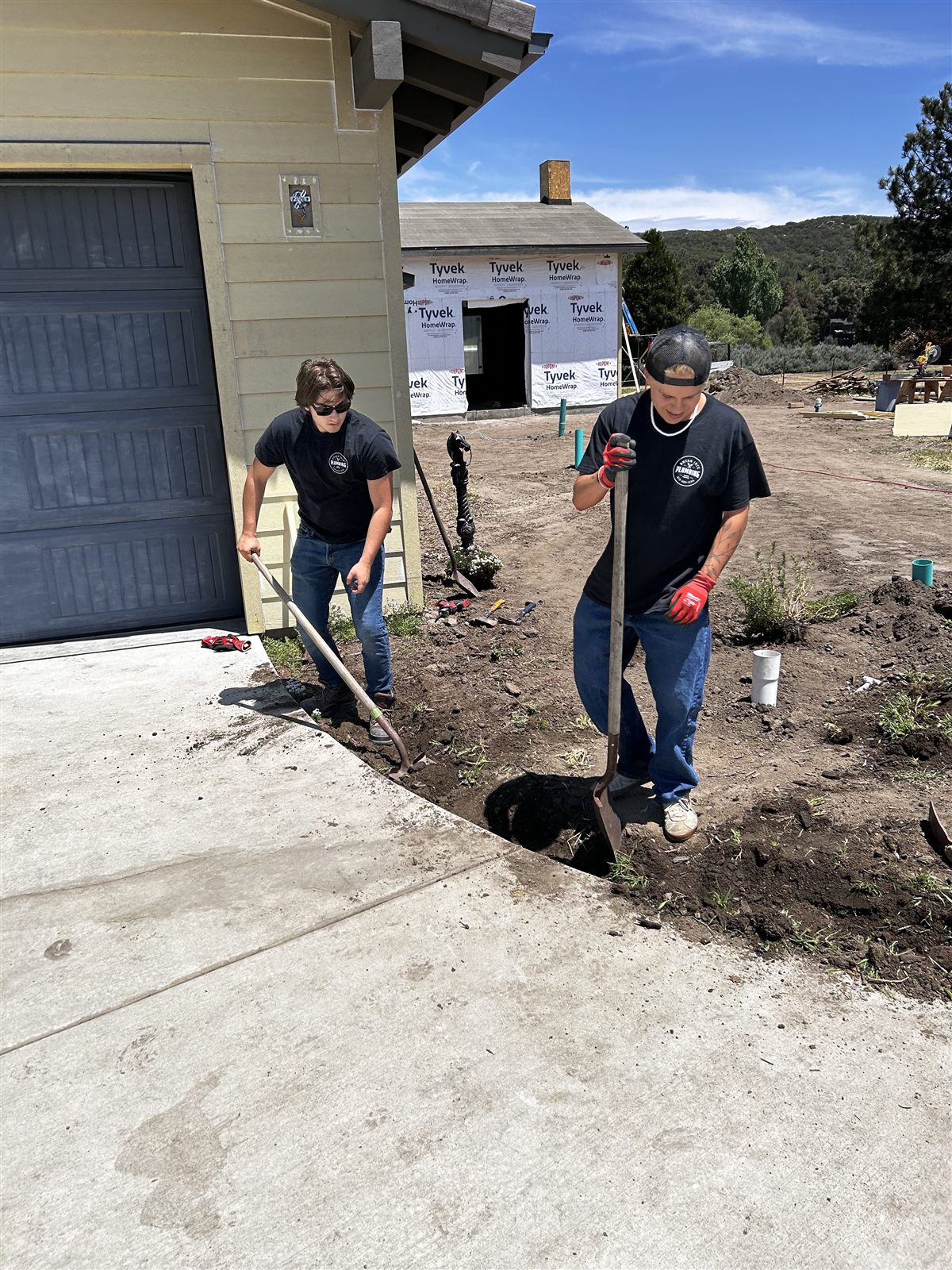 Two-person crew digging a plumbing trench at a new construction site